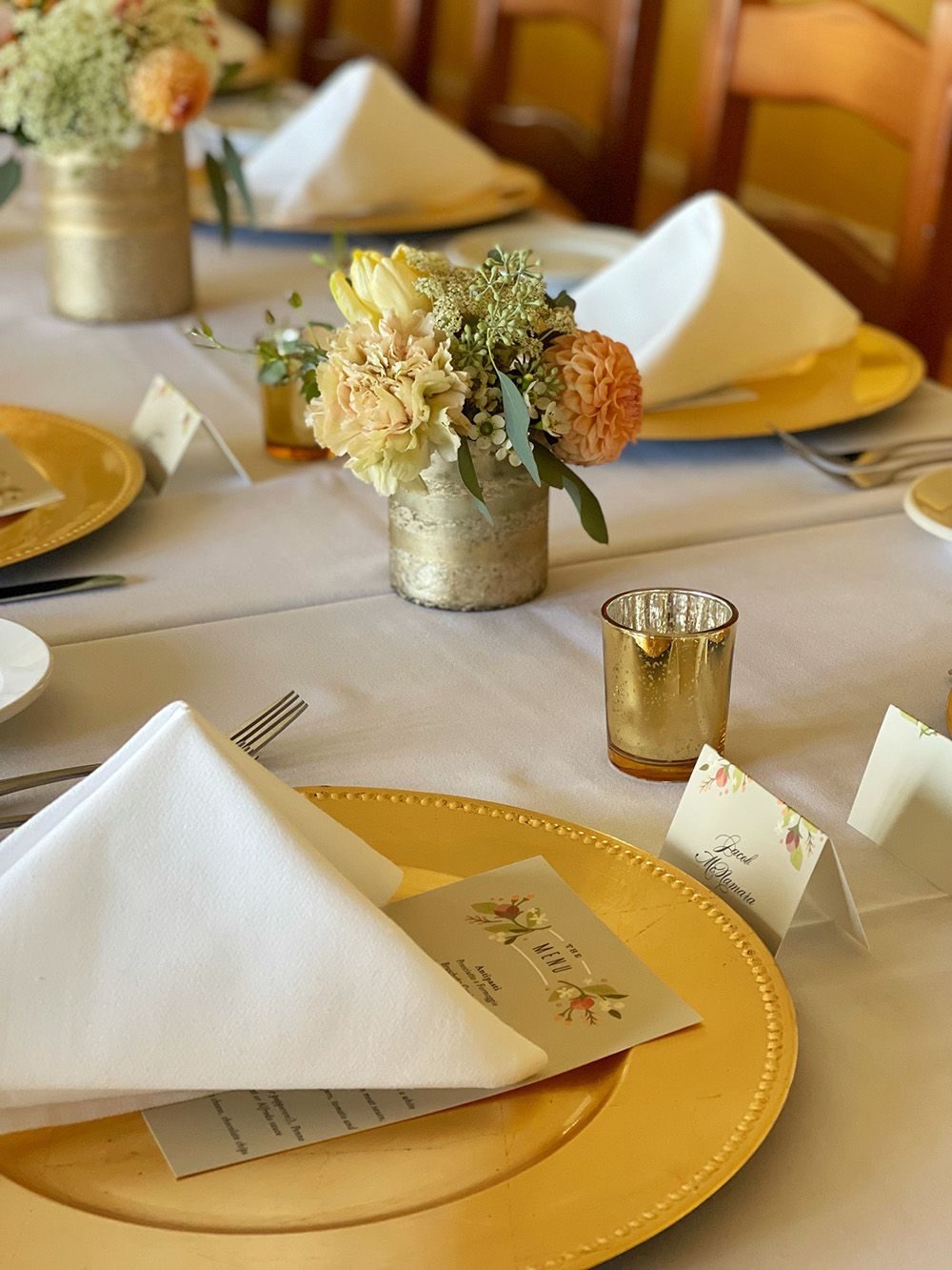 close up of banquet table with gold chargers, and pale yellow and orange flowers