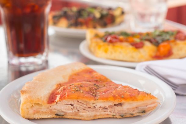 slice of turkey piadina with slices of pizza in background